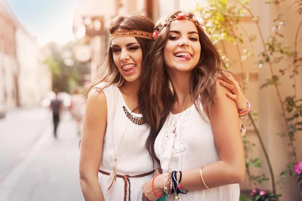 Two young women smiling and posing together in boho style outfits outdoors.