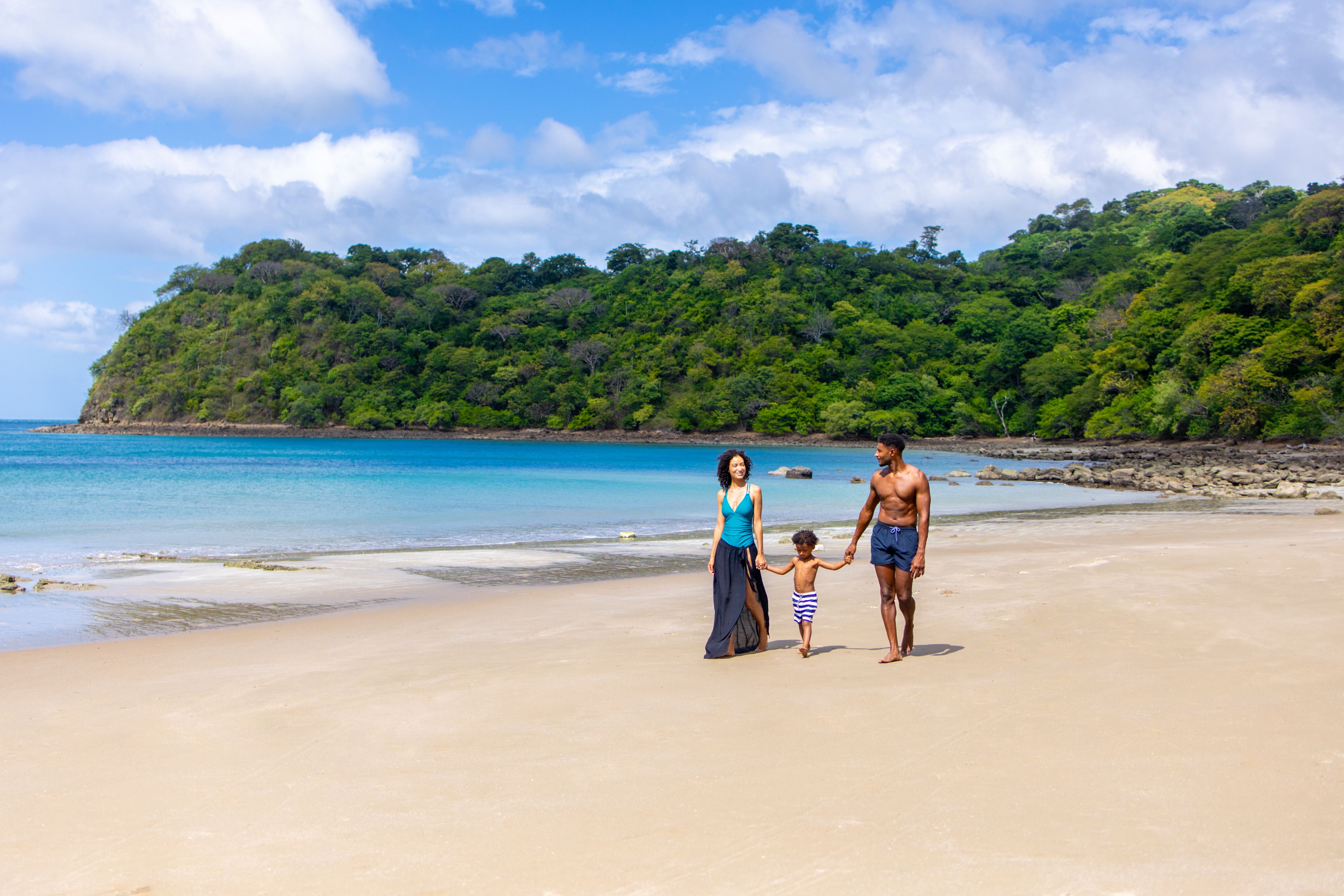 family walking on beach surrounded by tropical ocean shore and lush green land