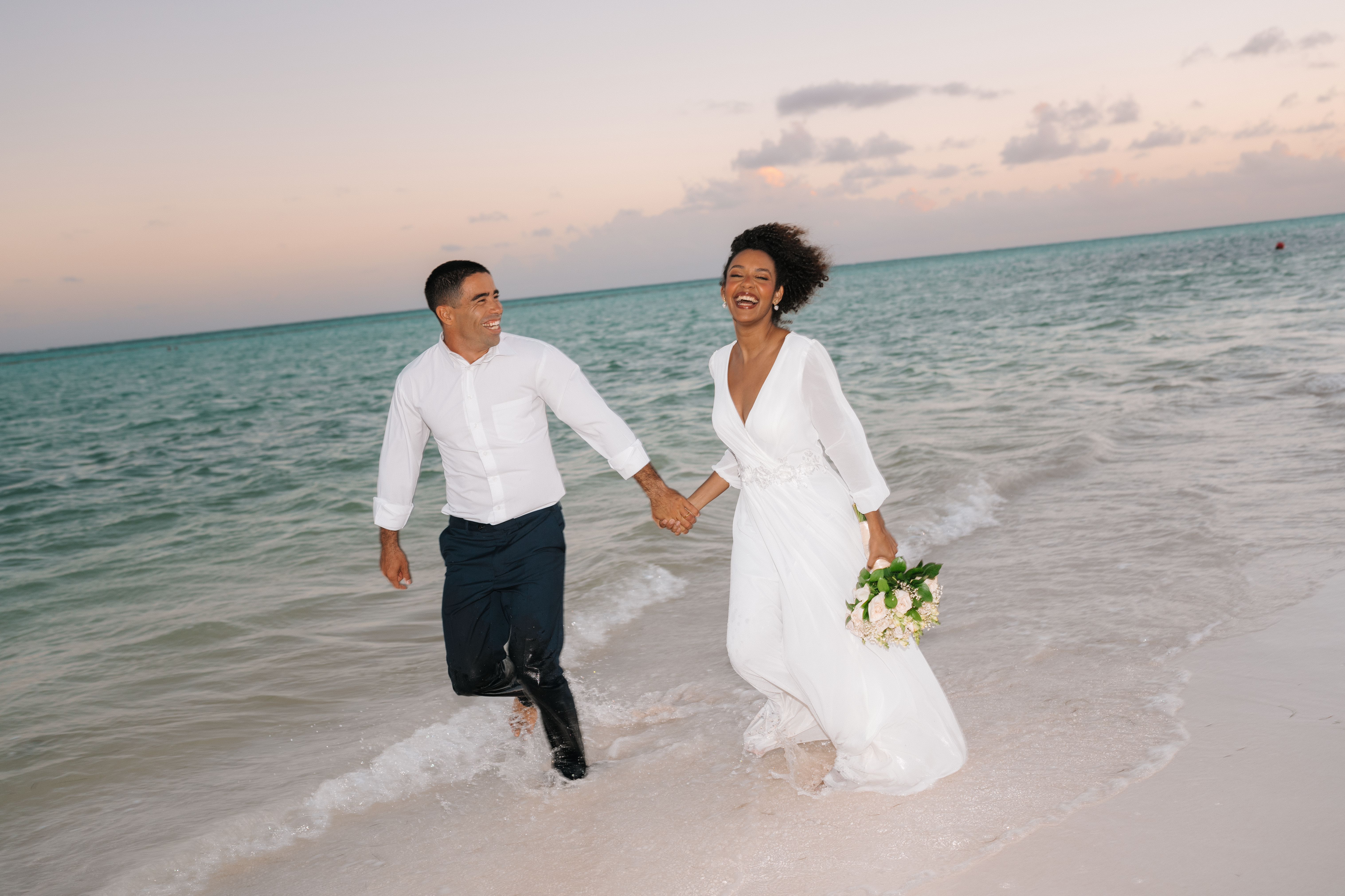 newlywed couple running along the shoreline with sunset in background