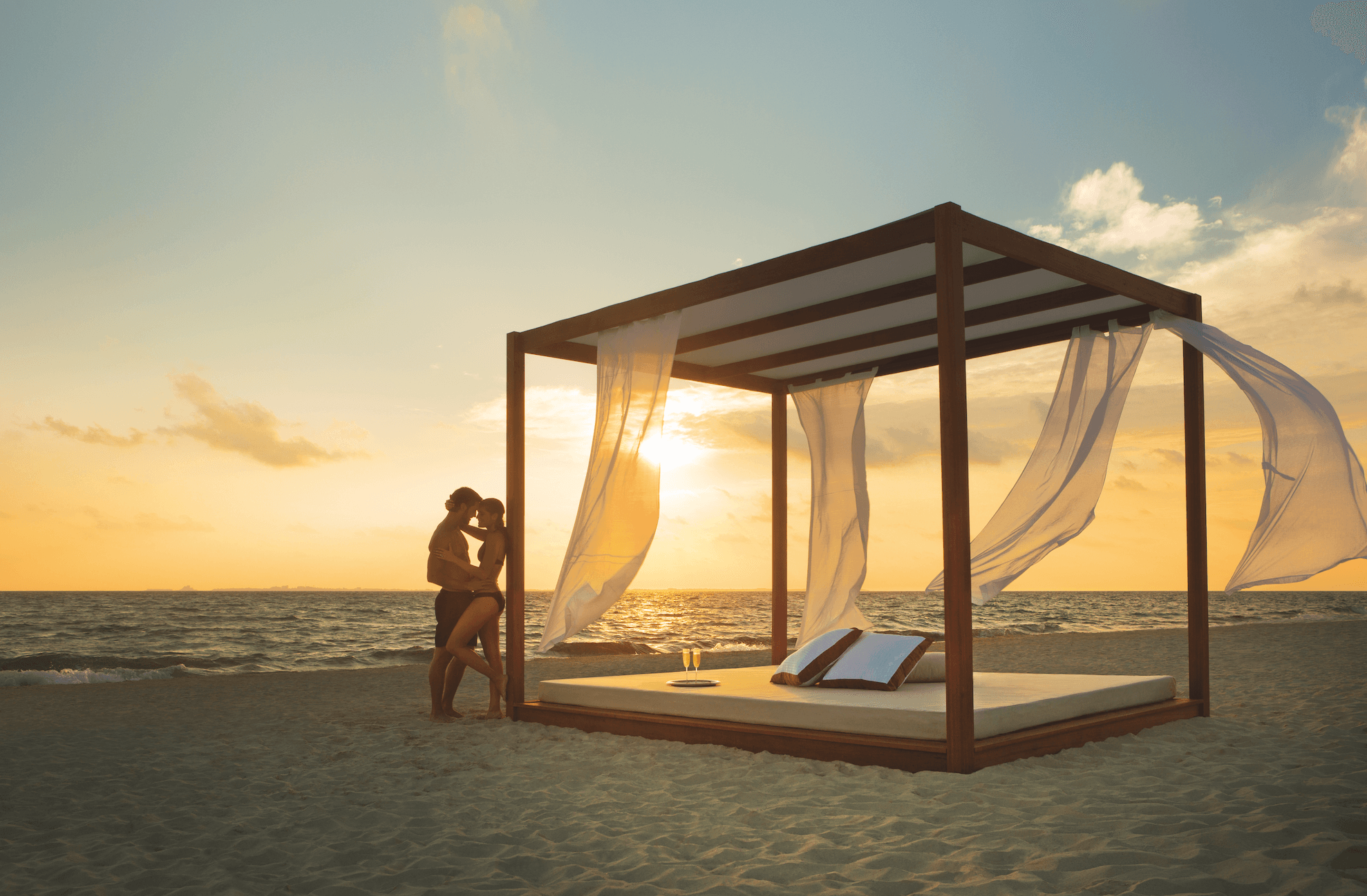 couple embracing against cabana on shoreline during sunset