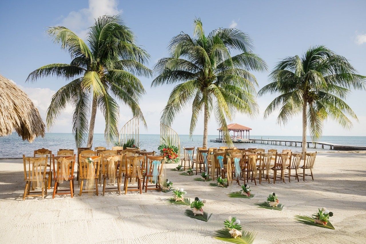 Beach wedding ceremony setup with wooden chairs, ribbons, a flower-lined aisle, and a display overlooking the ocean.