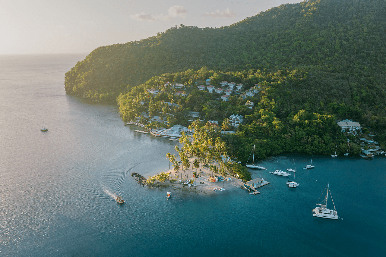 boats riding around a peninsula on the ocean that has a resort and lush greenery