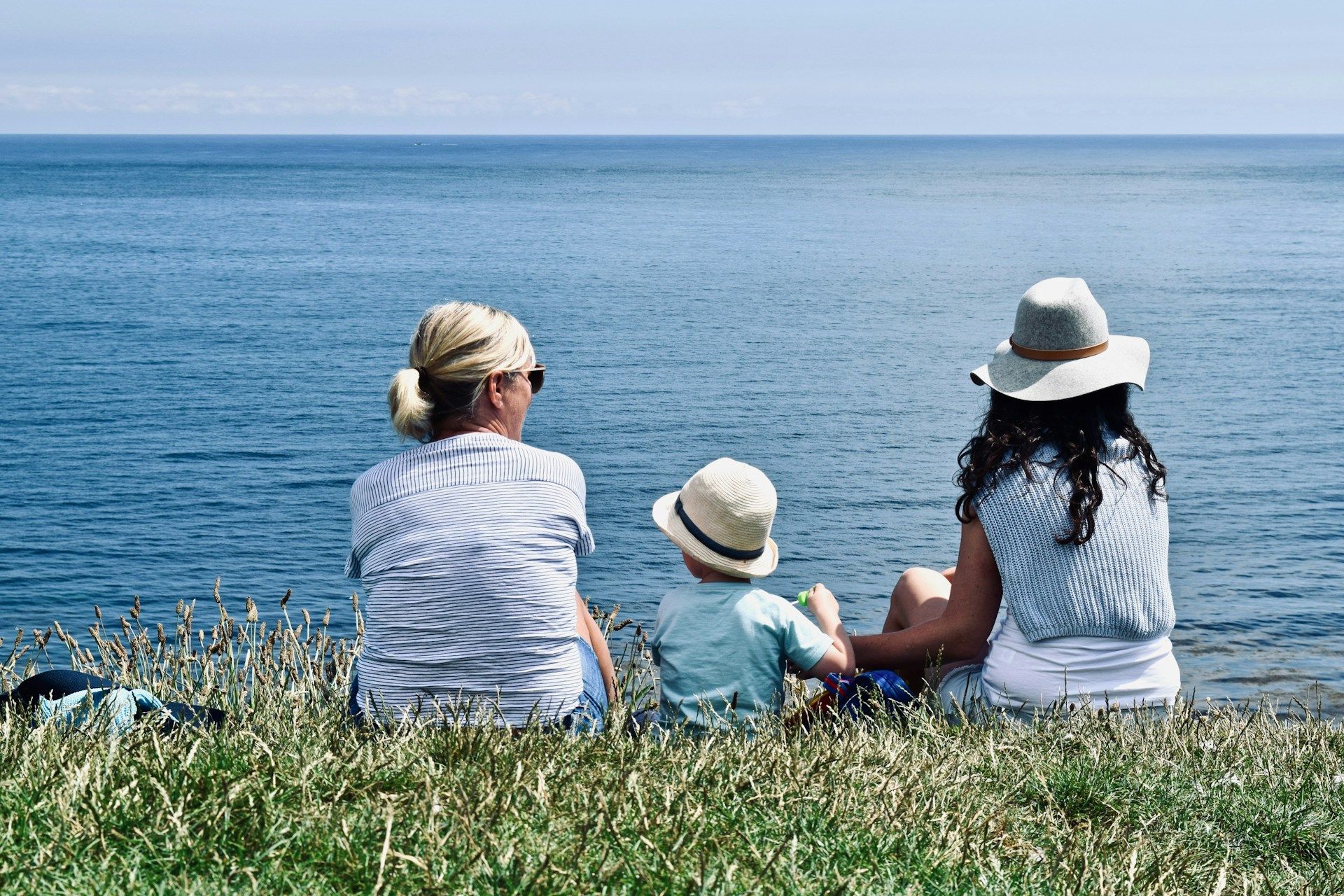 small child sitting on grass between two adults outlooking the ocean