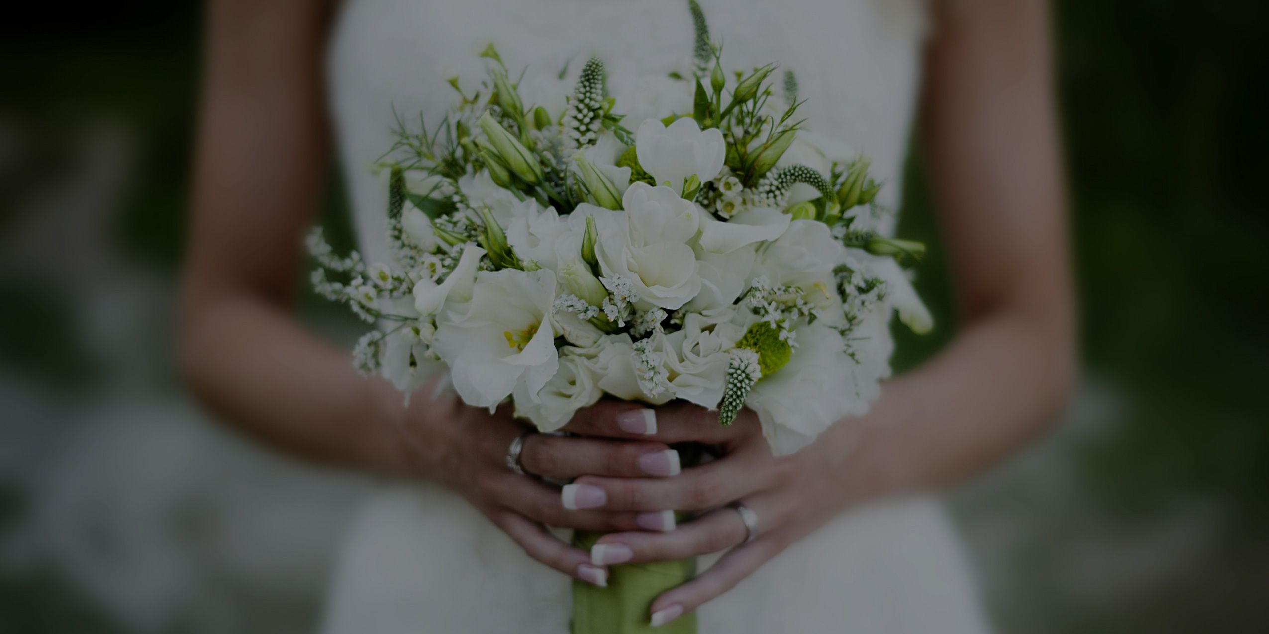Bride in white dress holding a bouquet of white flowers and greenery.