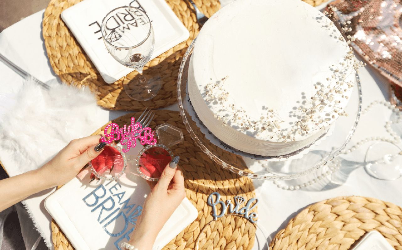 Bridal-themed table setup with a white cake, decorated place settings, and pink 'Bride to Be' sunglasses.
