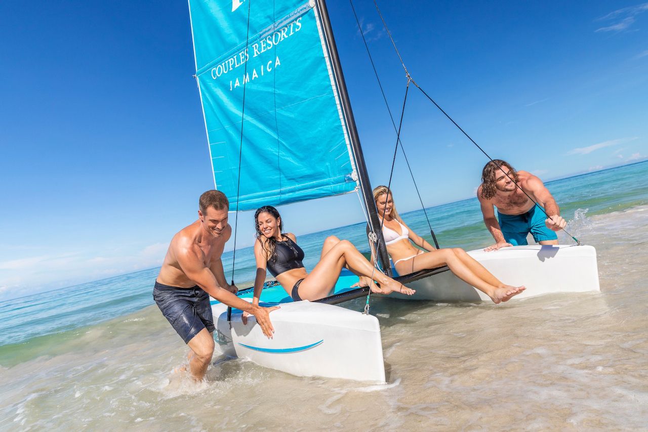 two women sitting on sailboat as two men push torward shore