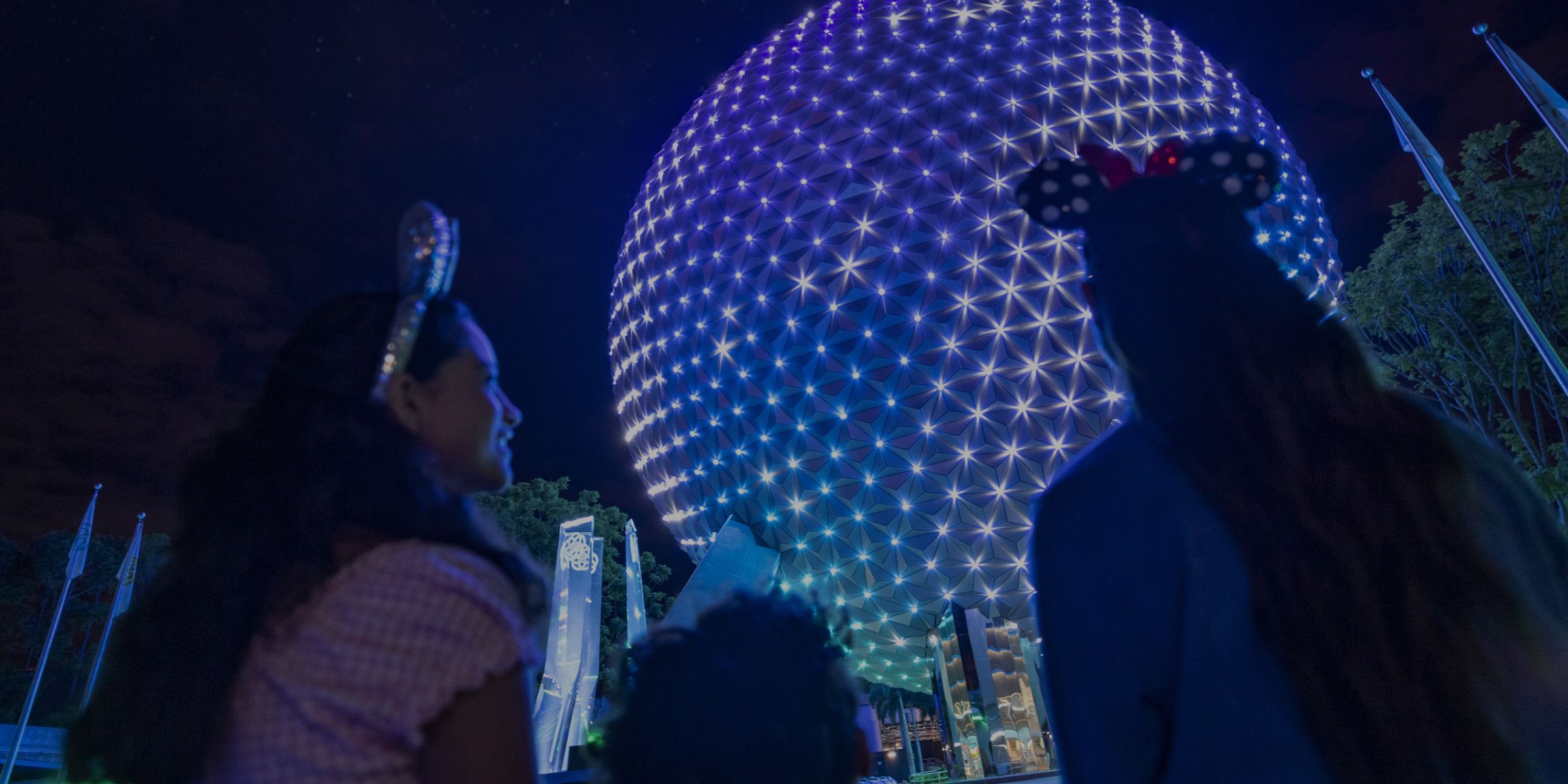 Family admiring EPCOT’s glowing Spaceship Earth at night