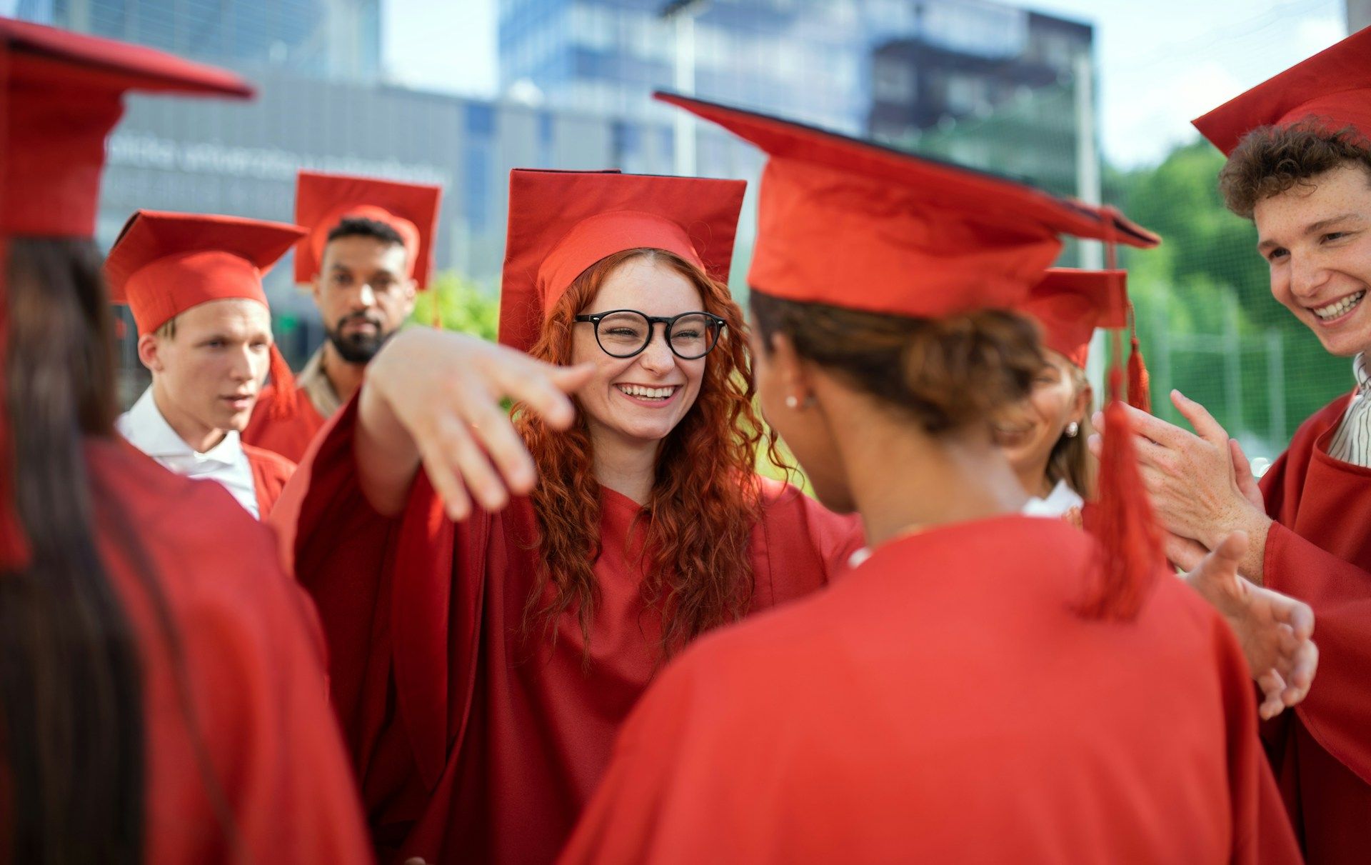 graduates in red cap and gowns hugging