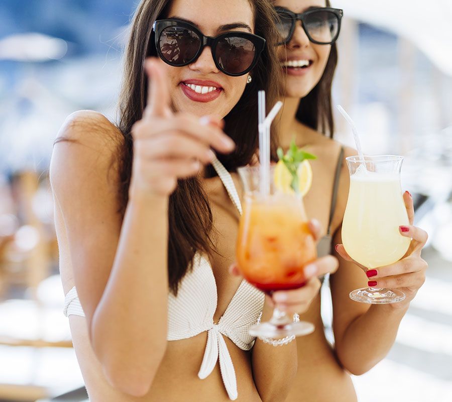 Two women in swimsuits enjoying cocktails and smiling poolside on vacation