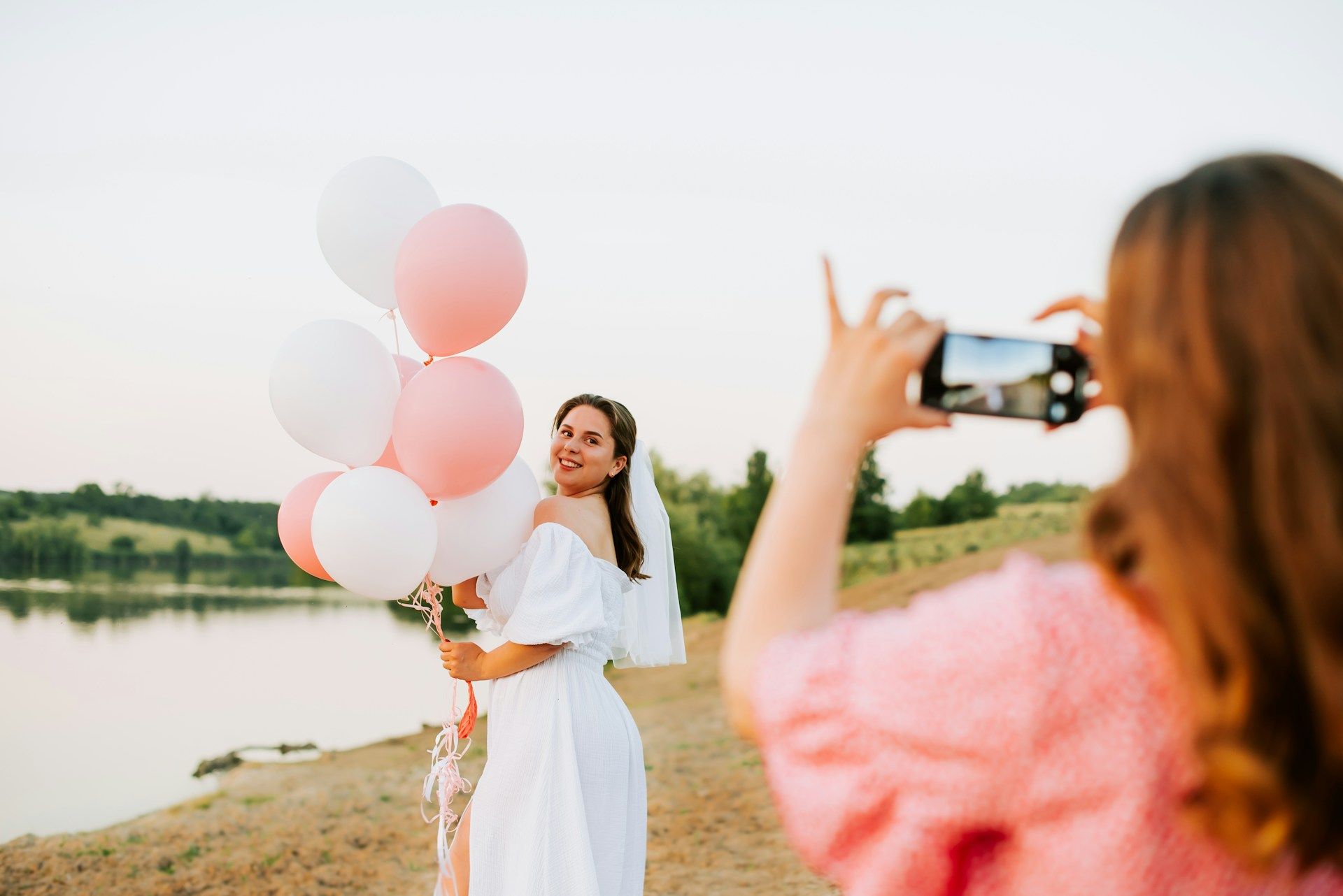 woman taking picture of bride holding pink and white balloons