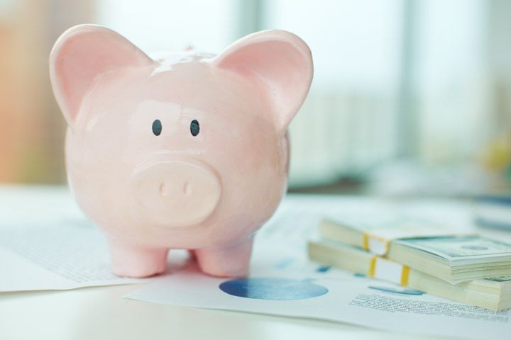 Pink piggy bank beside stacks of cash and financial documents on a desk.