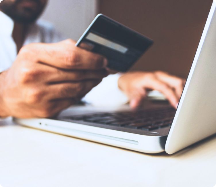 Hand holding credit card near laptop.