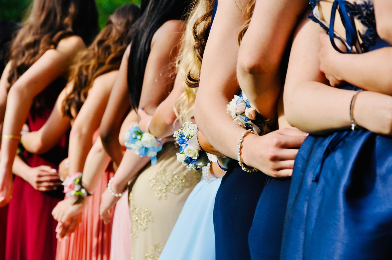 Group of friends in colorful dresses before prom standing side by side with corsages on their wrists.