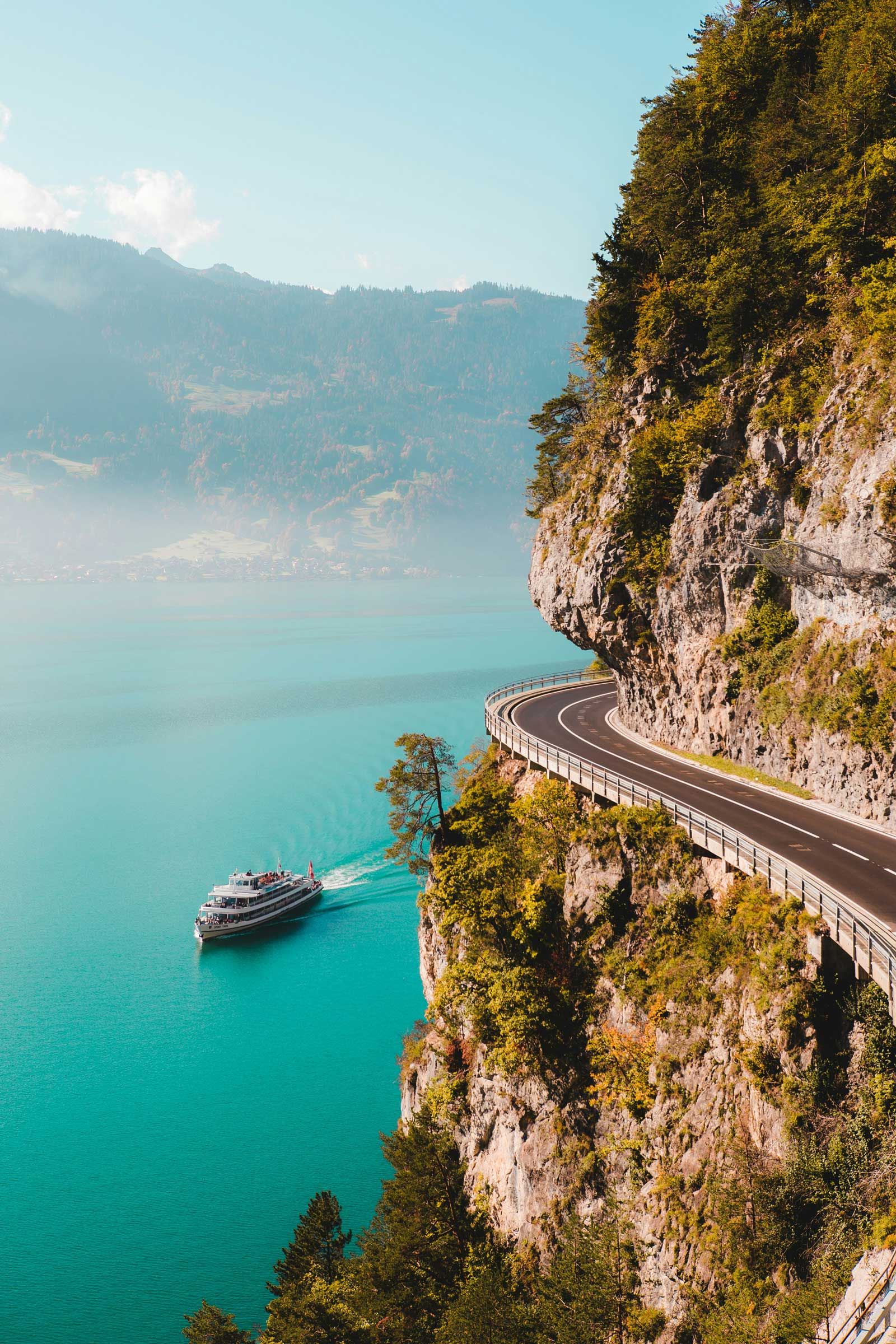 mountain road over coastline with boat moving across water